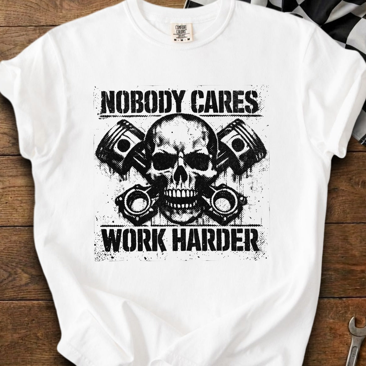 White t-shirt with a skull and pistons graphic reading "NOBODY CARES WORK HARDER."