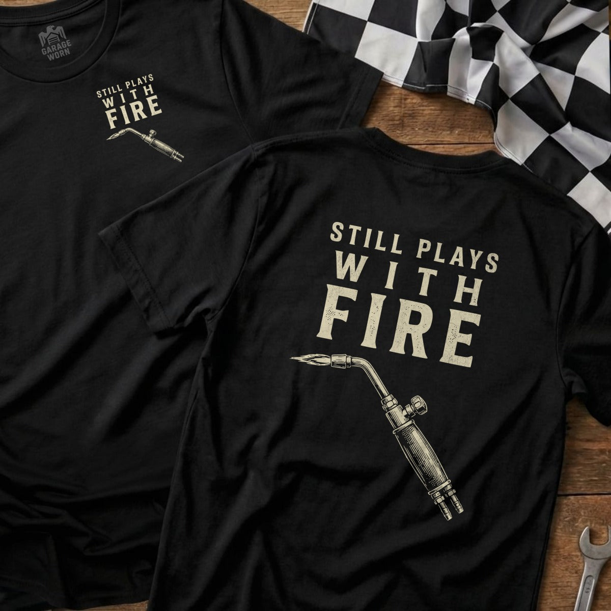 Black t-shirt with "STILL PLAYS WITH FIRE" and a blowtorch graphic.