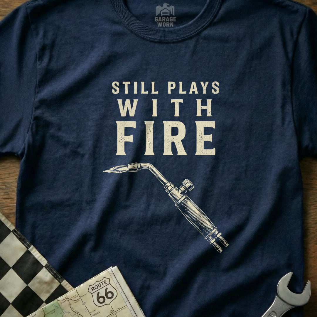 Navy t-shirt with "Still Plays With Fire" and a welding torch graphic.