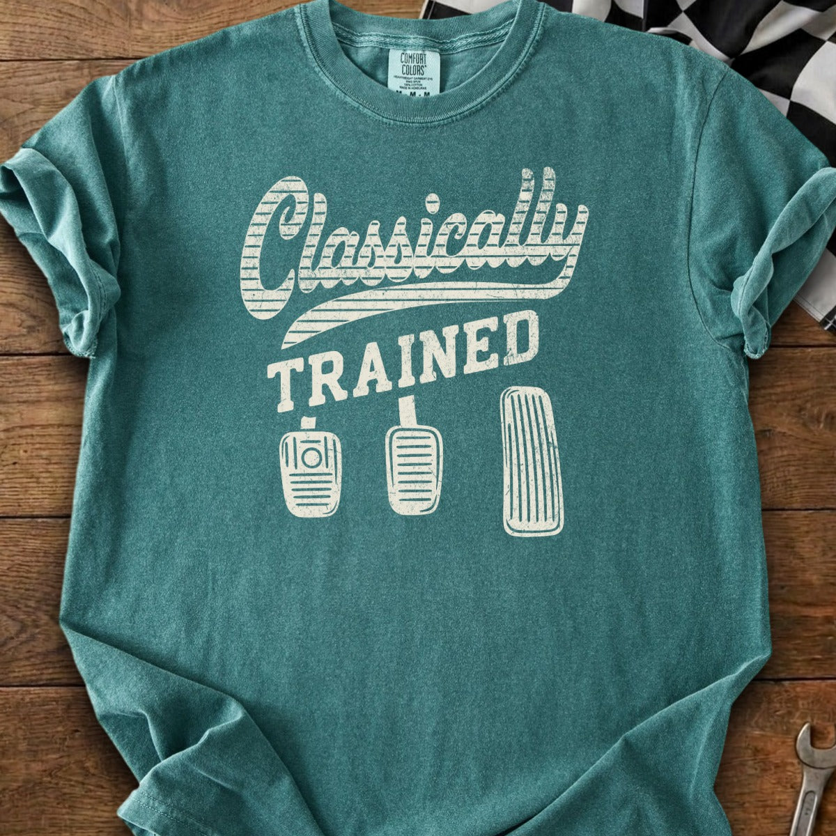 Teal t-shirt with "Classically TRAINED" and three car pedals graphic.