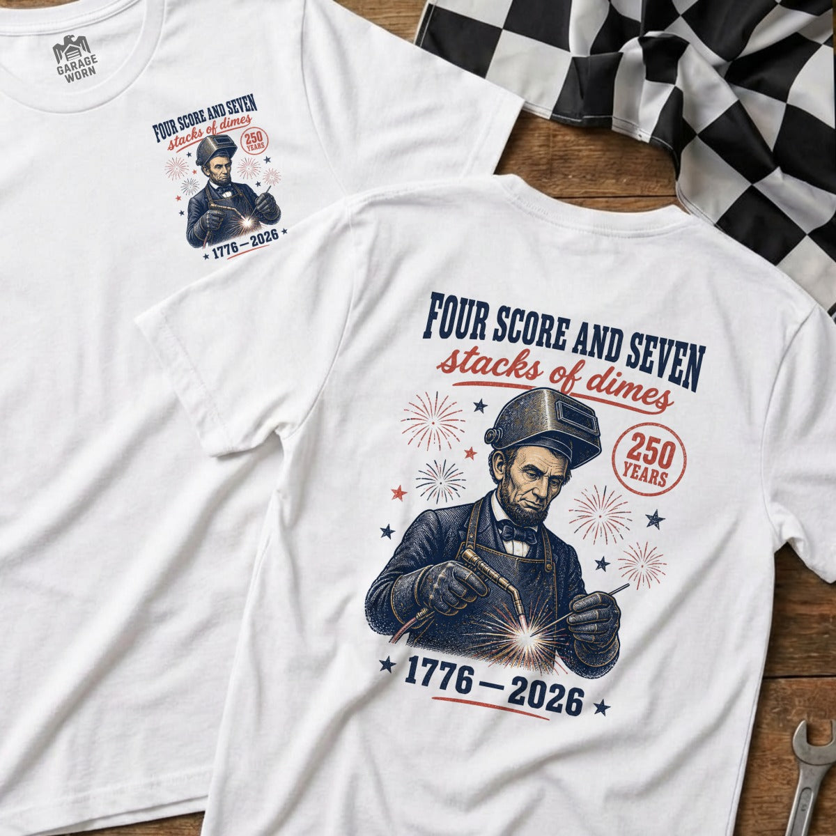 White t-shirt with Abraham Lincoln welding, text "Four score and seven stacks of dimes 1776-2026".