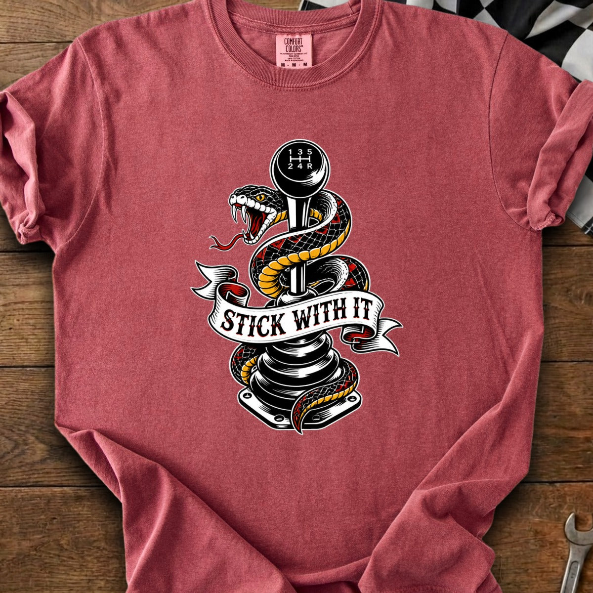 Snake coiled around a manual transmission stick shift with "STICK WITH IT" text.