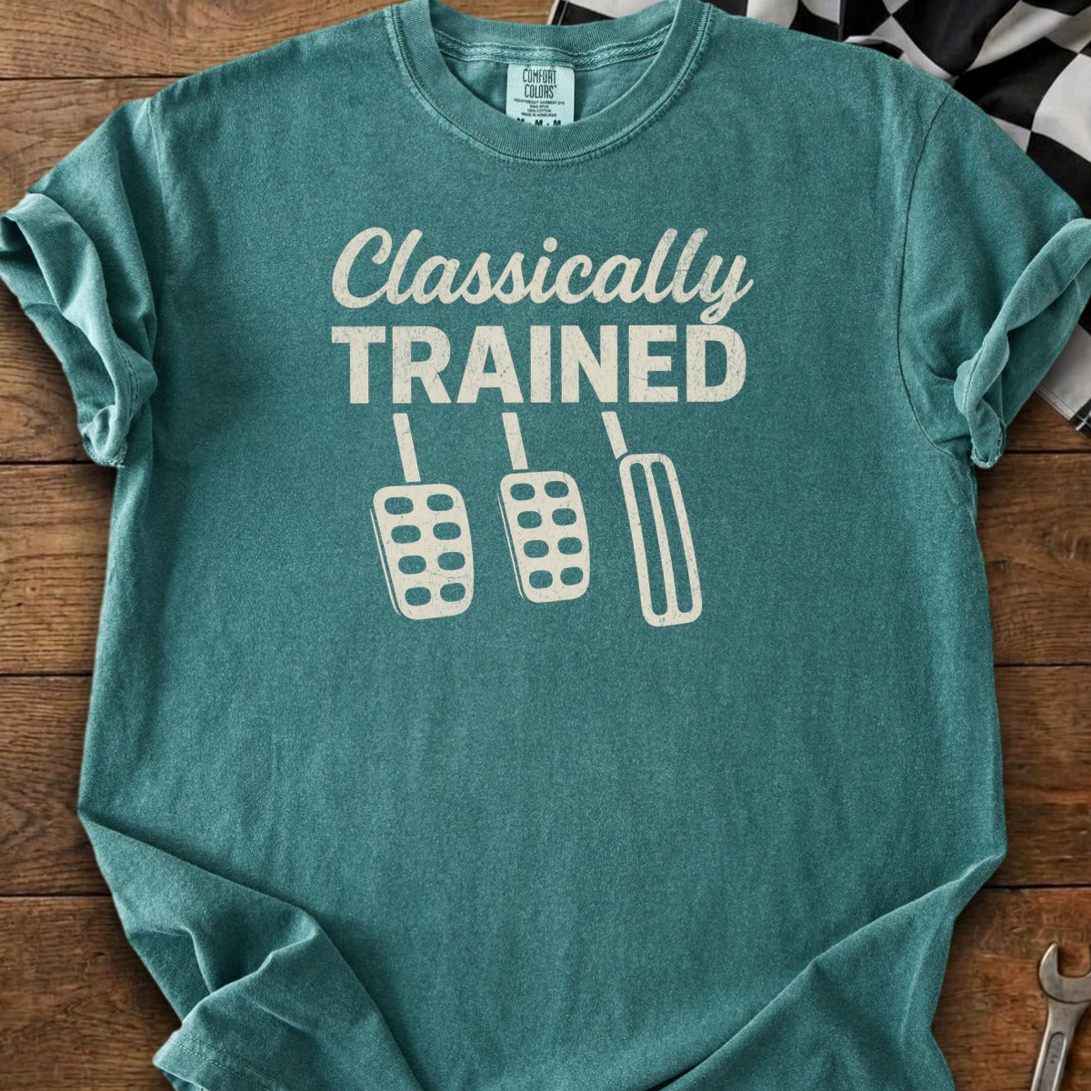 Teal t-shirt with "Classically TRAINED" and three manual car pedals.