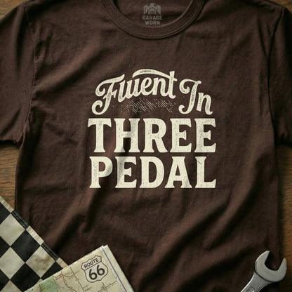 Brown t-shirt with white text "Fluent In THREE PEDAL" and Route 66 map.