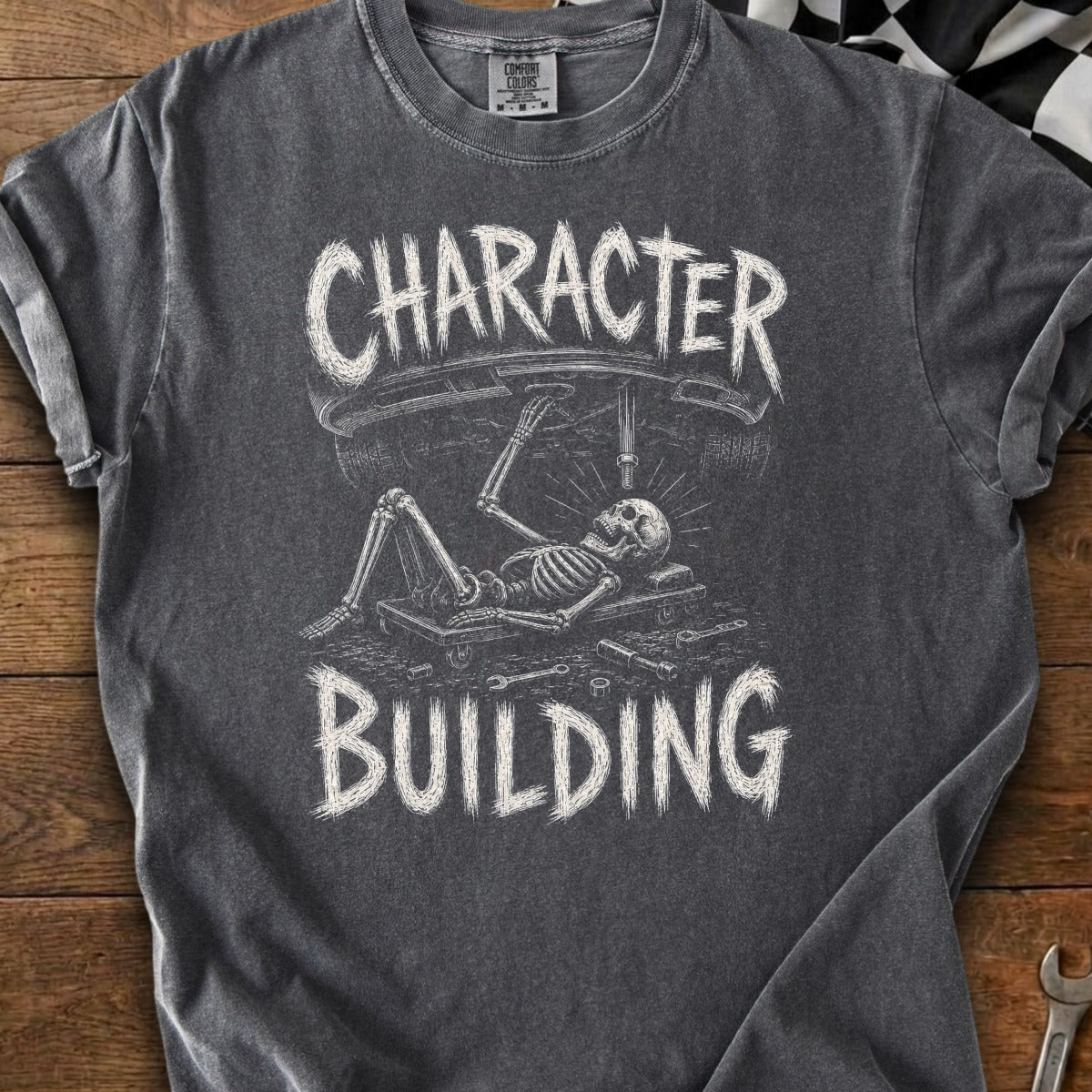 Skeleton working on a car with text "CHARACTER BUILDING" on a dark t-shirt.