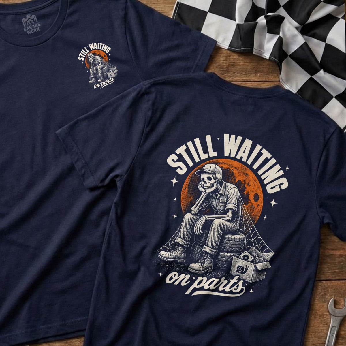 Navy t-shirt with skeleton sitting on tires, text "Still Waiting On Parts."