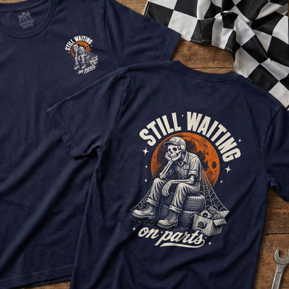 Navy t-shirt with skeleton sitting on tires, text "Still Waiting On Parts."