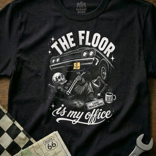 Black t-shirt with skeleton working on car below, "The floor is my office."