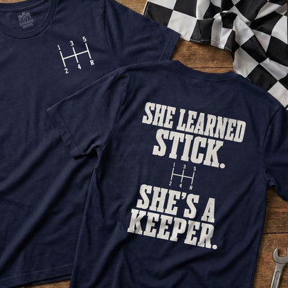 Navy t-shirt with a 5-speed gear shift pattern and "She Learned Stick" text.