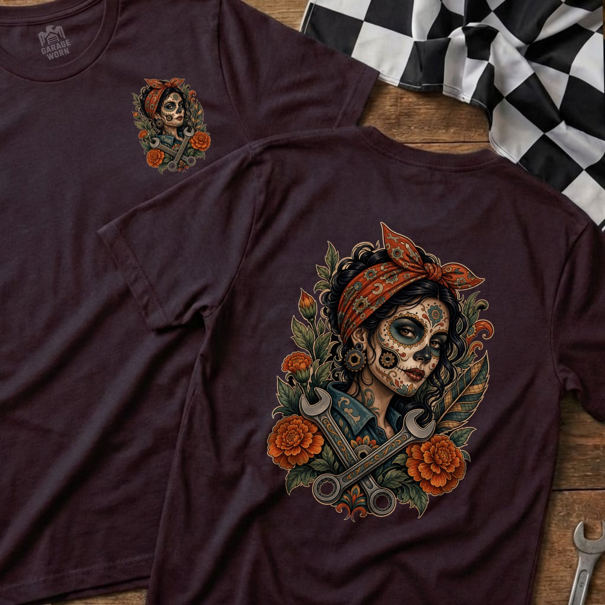 Dark t-shirt with sugar skull mechanic woman art, orange flowers, and wrenches.