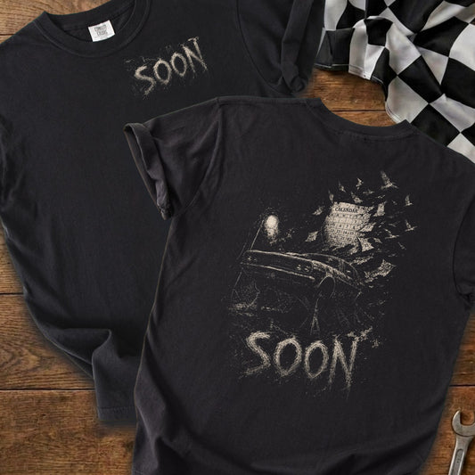 Black t-shirt with "SOON" graphic on front, and car, calendar, birds graphic on back.