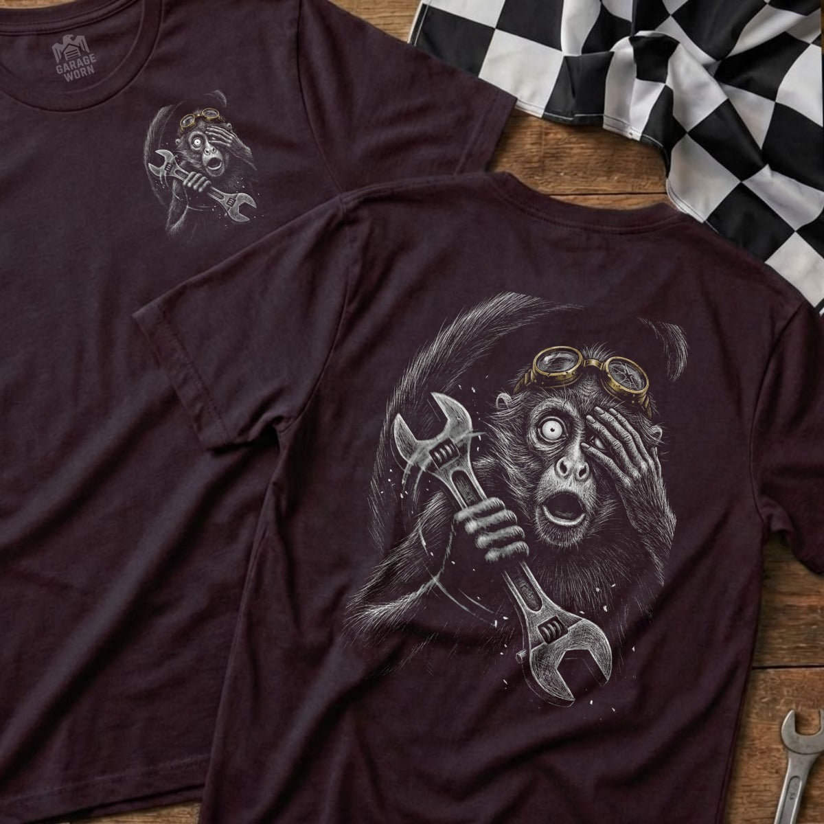 Graphic t-shirt with a startled monkey holding a wrench, on a wooden surface.