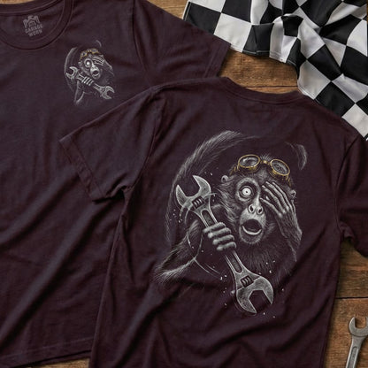 Graphic t-shirt with a startled monkey holding a wrench, on a wooden surface.