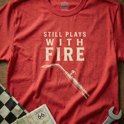 Red t-shirt with "STILL PLAYS WITH FIRE" and a welding torch graphic.
