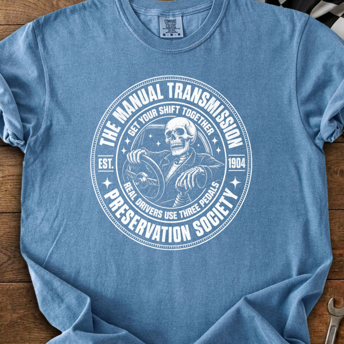T-shirt with circular graphic featuring a skeleton driving, "Manual Transmission Preservation Society" text.