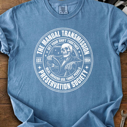 T-shirt with circular graphic featuring a skeleton driving, "Manual Transmission Preservation Society" text.