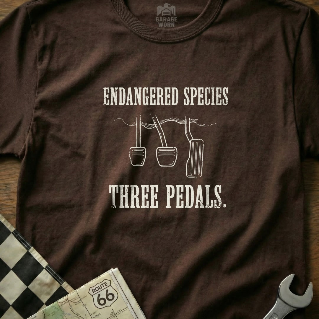 Brown t-shirt with "Endangered Species Three Pedals" and a clutch pedal graphic.