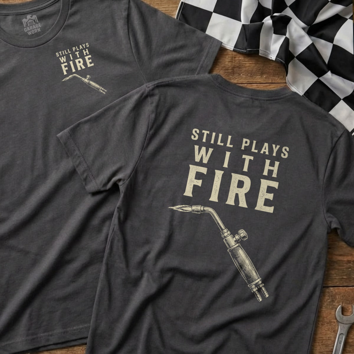 Dark t-shirt with "STILL PLAYS WITH FIRE" and a blow torch graphic.