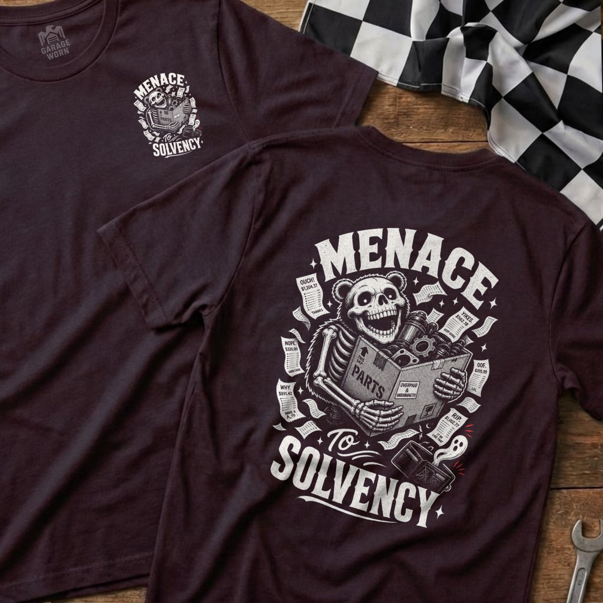 Dark t-shirt with skeleton bear holding a box of parts, surrounded by bills labeled "MENACE TO SOLVENCY".