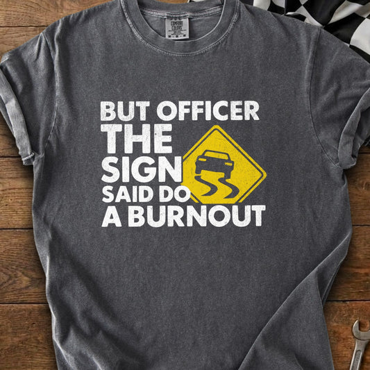 Dark grey t-shirt with white text reading "BUT OFFICER THE SIGN SAID DO A BURNOUT" and a yellow slippery road sign.