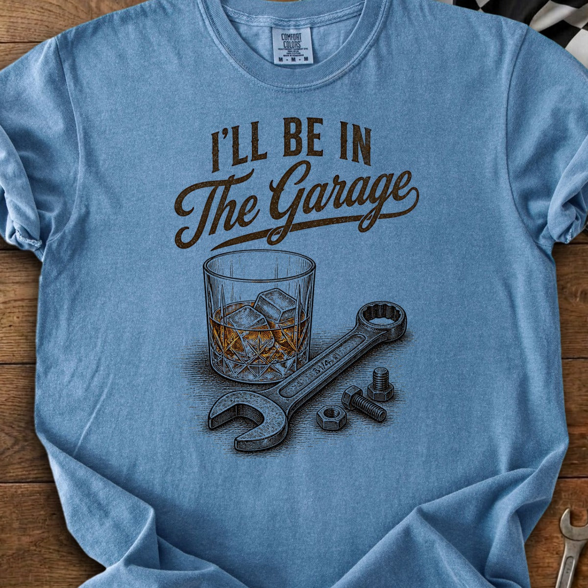 Blue t-shirt with "I’ll be in The Garage" text, whiskey glass, wrench, nuts, and bolts.