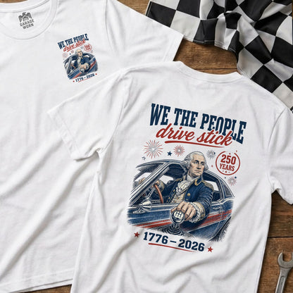 White t-shirt featuring George Washington driving with text "WE THE PEOPLE drive stick 1776-2026".
