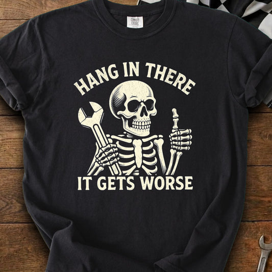 Skeleton graphic with text "HANG IN THERE IT GETS WORSE" on a black t-shirt.