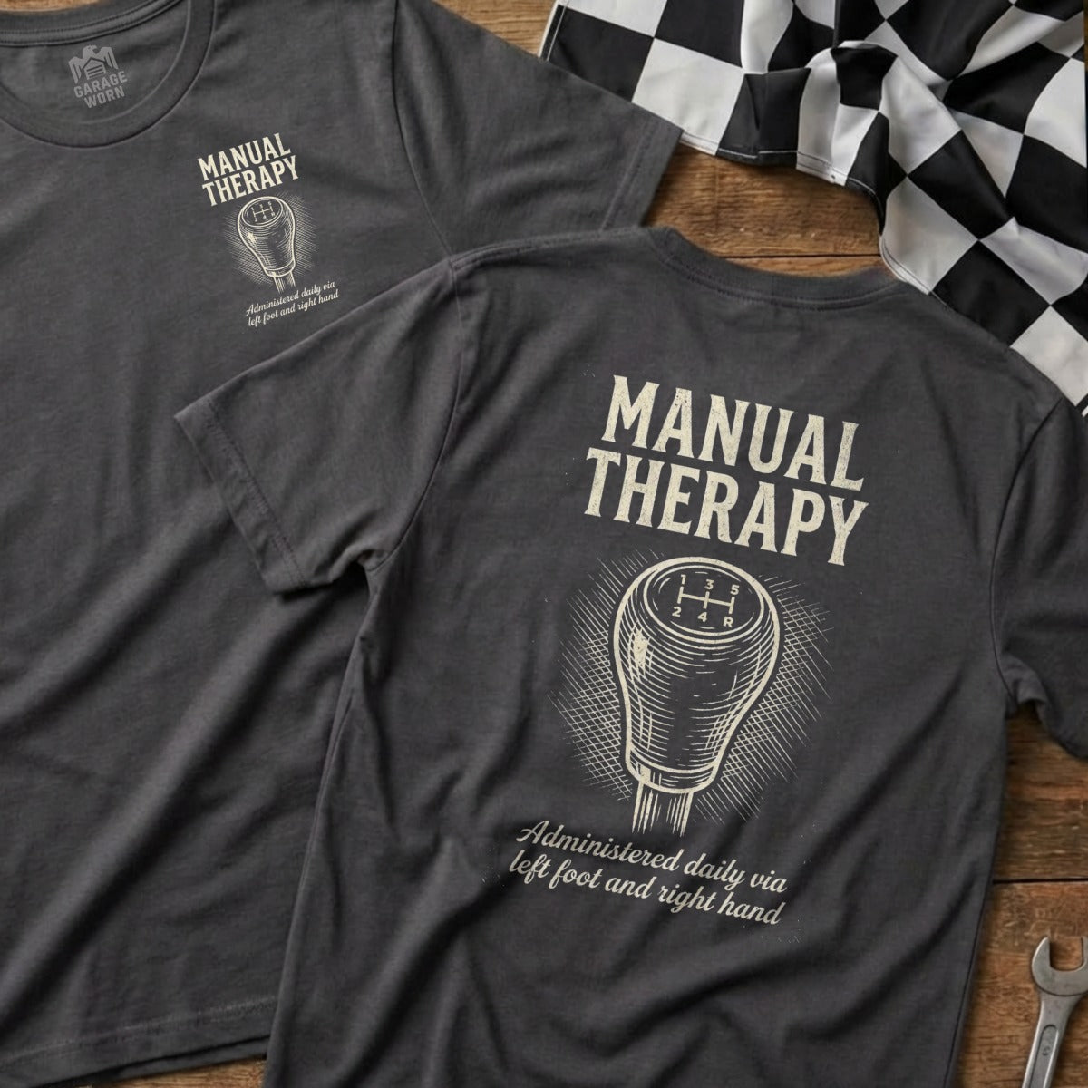 Dark grey t-shirt with "Manual Therapy" and gear shift graphic, with text.