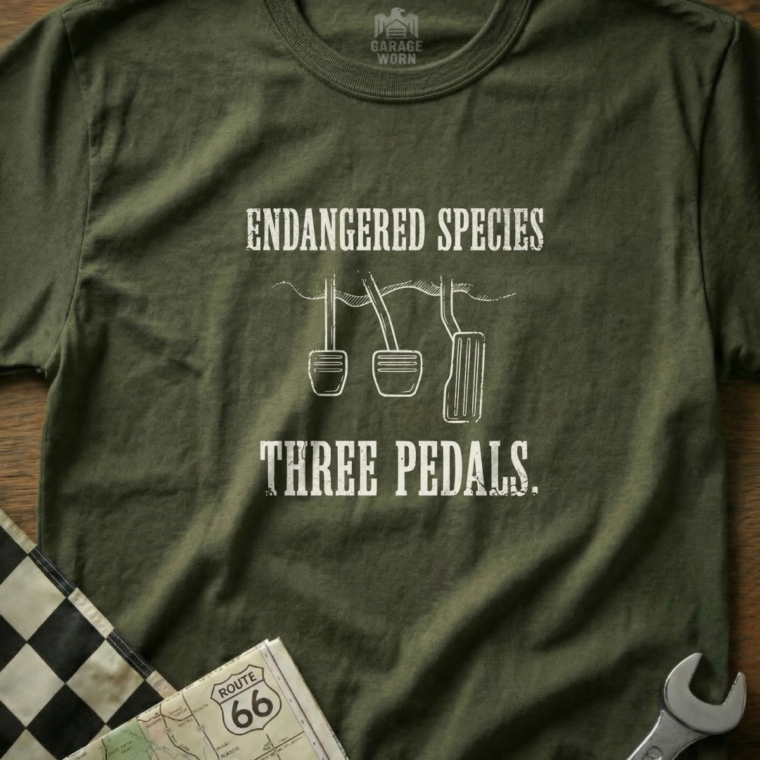 Olive green t-shirt with "Endangered Species Three Pedals" text and car pedal graphics.