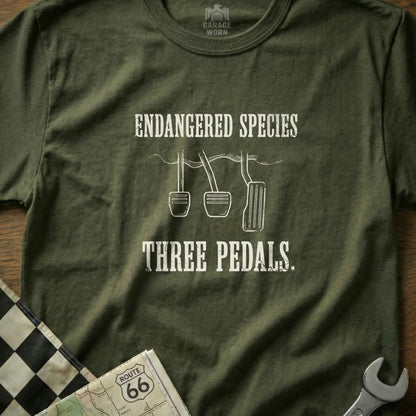 Olive green t-shirt with "Endangered Species Three Pedals" text and car pedal graphics.