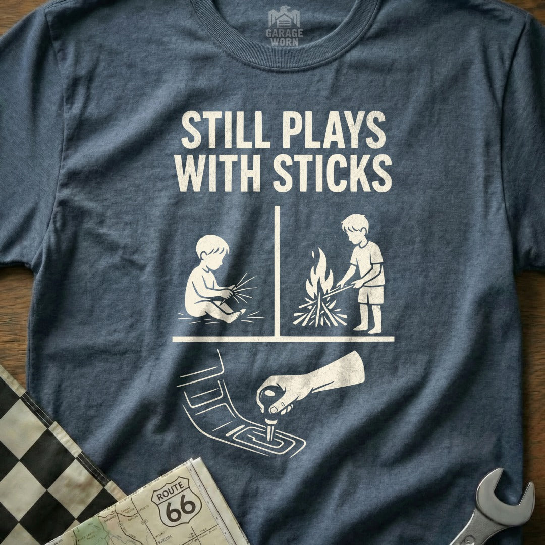 T-shirt with graphic depicting a baby playing with sticks and a child by a campfire.