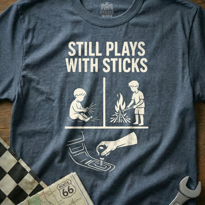 T-shirt with graphic depicting a baby playing with sticks and a child by a campfire.