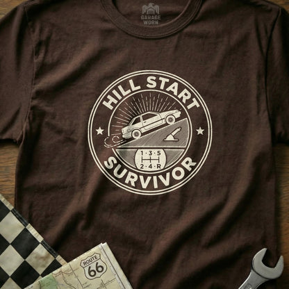 Brown t-shirt with "Hill Start Survivor" graphic and car on a slope.