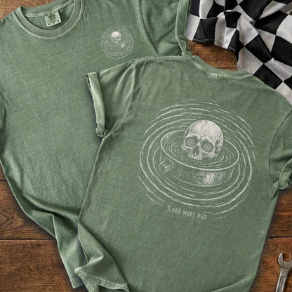 Green t-shirt with skull absorbing ripples and text "OIL DRAIN 3,000 MILES AGO".