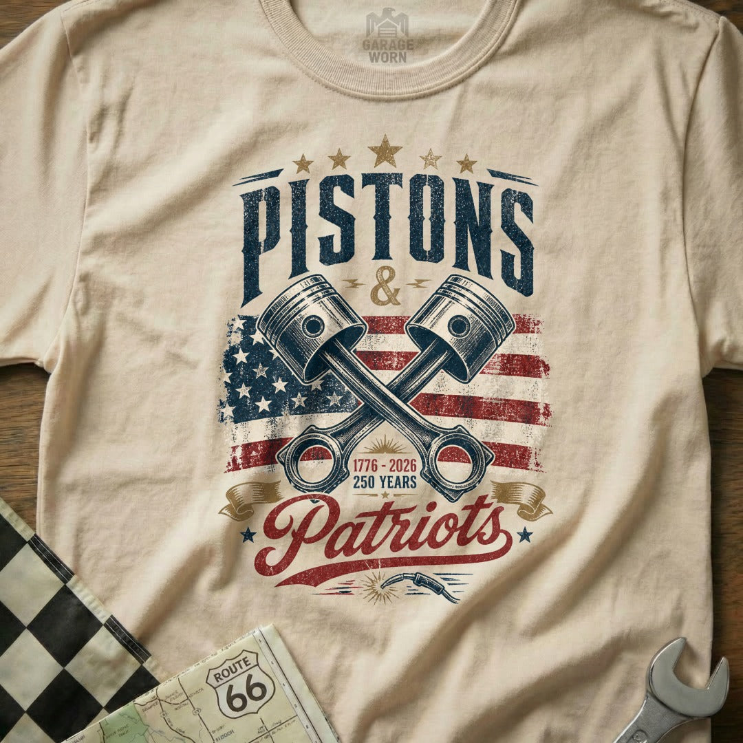 Cream t-shirt with "Pistons & Patriots", crossed pistons, and US flag graphic.