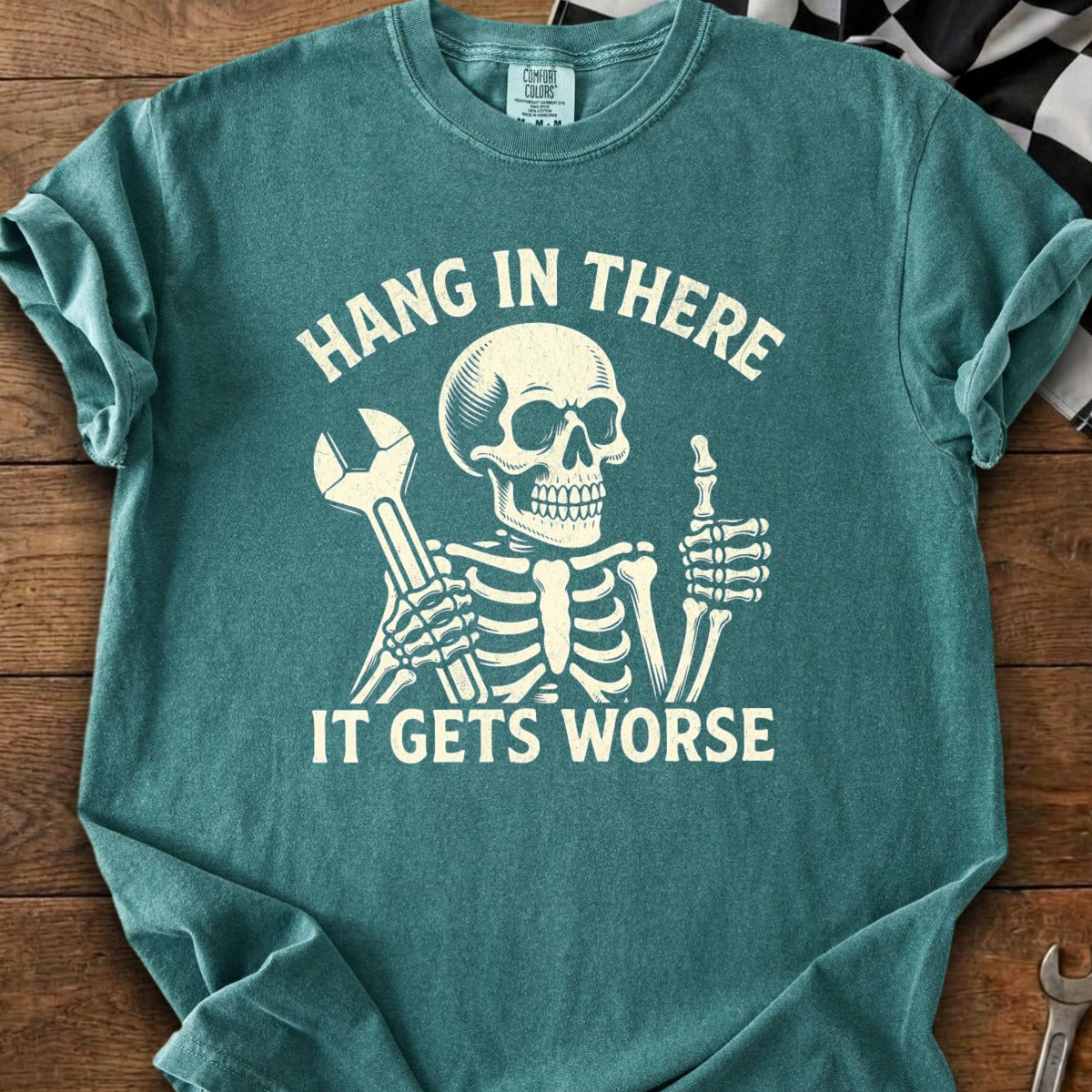 Skeleton graphic on teal t-shirt with text "HANG IN THERE IT GETS WORSE".