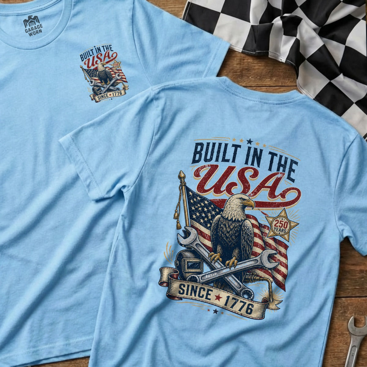 Light blue t-shirt with "Built in the USA" graphic featuring eagle, flag, and wrenches.