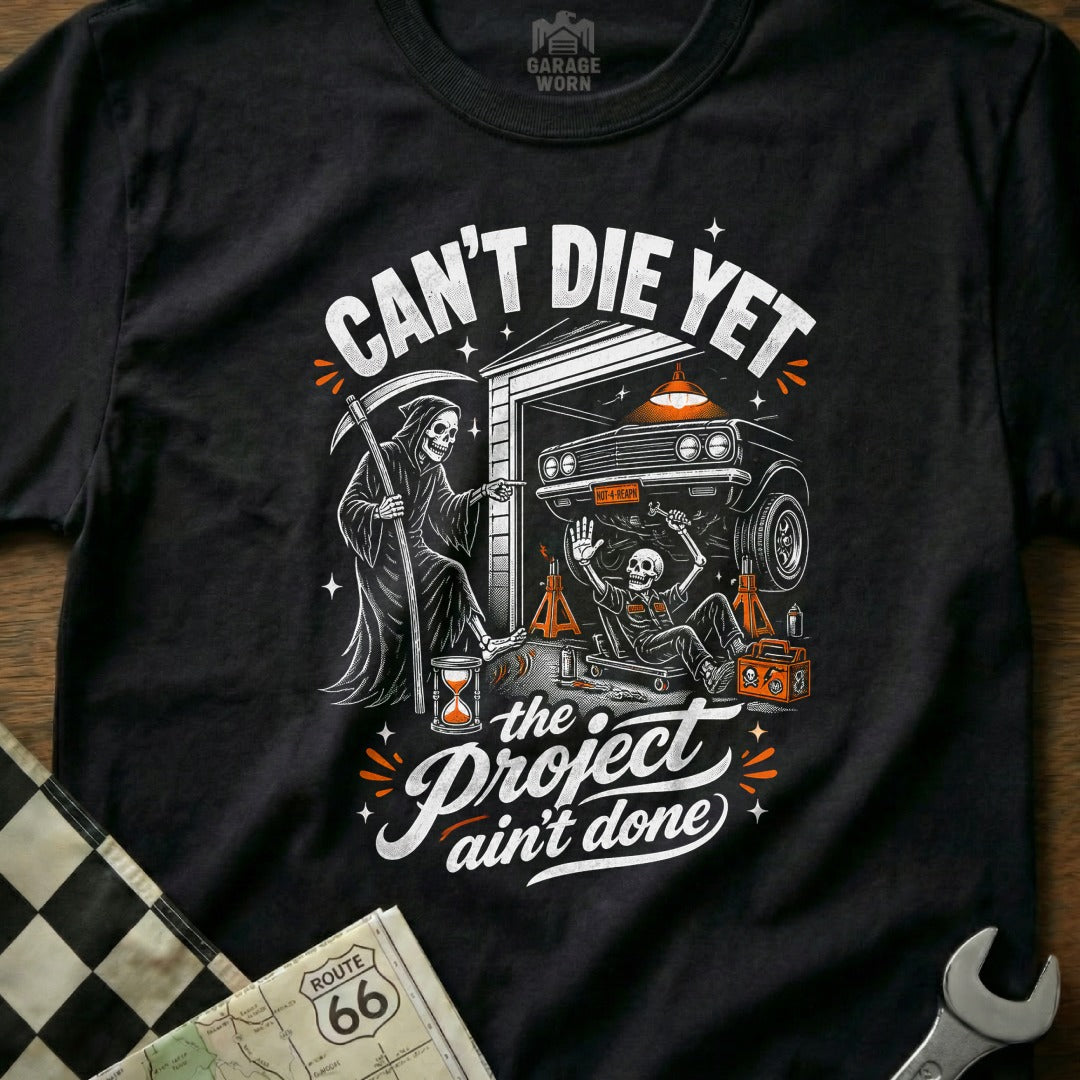 Grim Reaper and skeleton working on a car, "Can't Die Yet" and "Project Ain't Done."