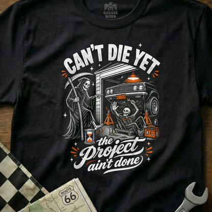 Grim Reaper and skeleton working on a car, "Can't Die Yet" and "Project Ain't Done."
