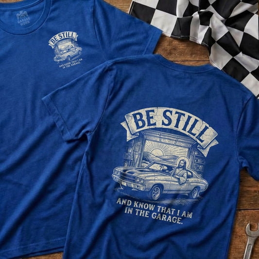 Blue t-shirt with Jesus driving a classic car and text: "Be Still and Know That I Am in the Garage."
