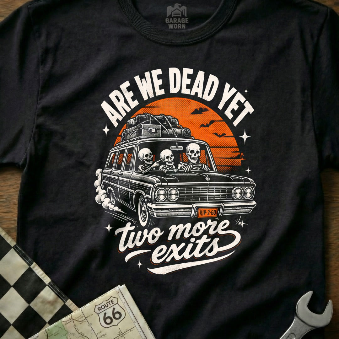 Black t-shirt with skeletons in a car, "ARE WE DEAD YET" and "two more exits" text.