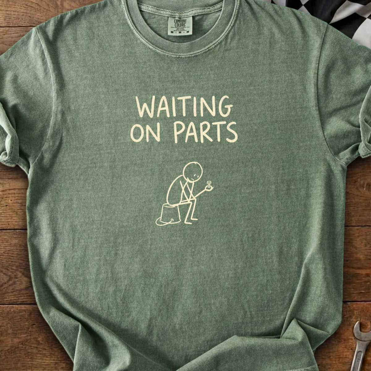 Green t-shirt graphic with text "WAITING ON PARTS" and a stick figure holding a gear.