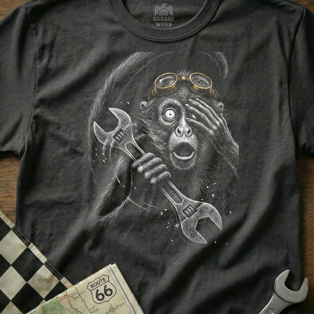 Monkey in goggles holding wrenches, hand over eye, on charcoal t-shirt.