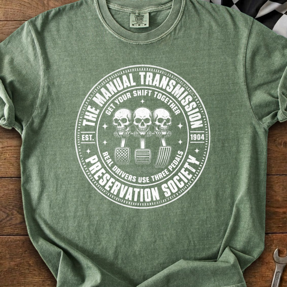 Green t-shirt with white graphic of three skulls on gear shift and text "The Manual Transmission Preservation Society".