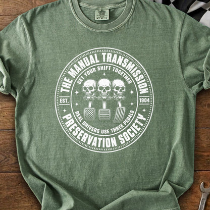Green t-shirt with white graphic of three skulls on gear shift and text "The Manual Transmission Preservation Society".