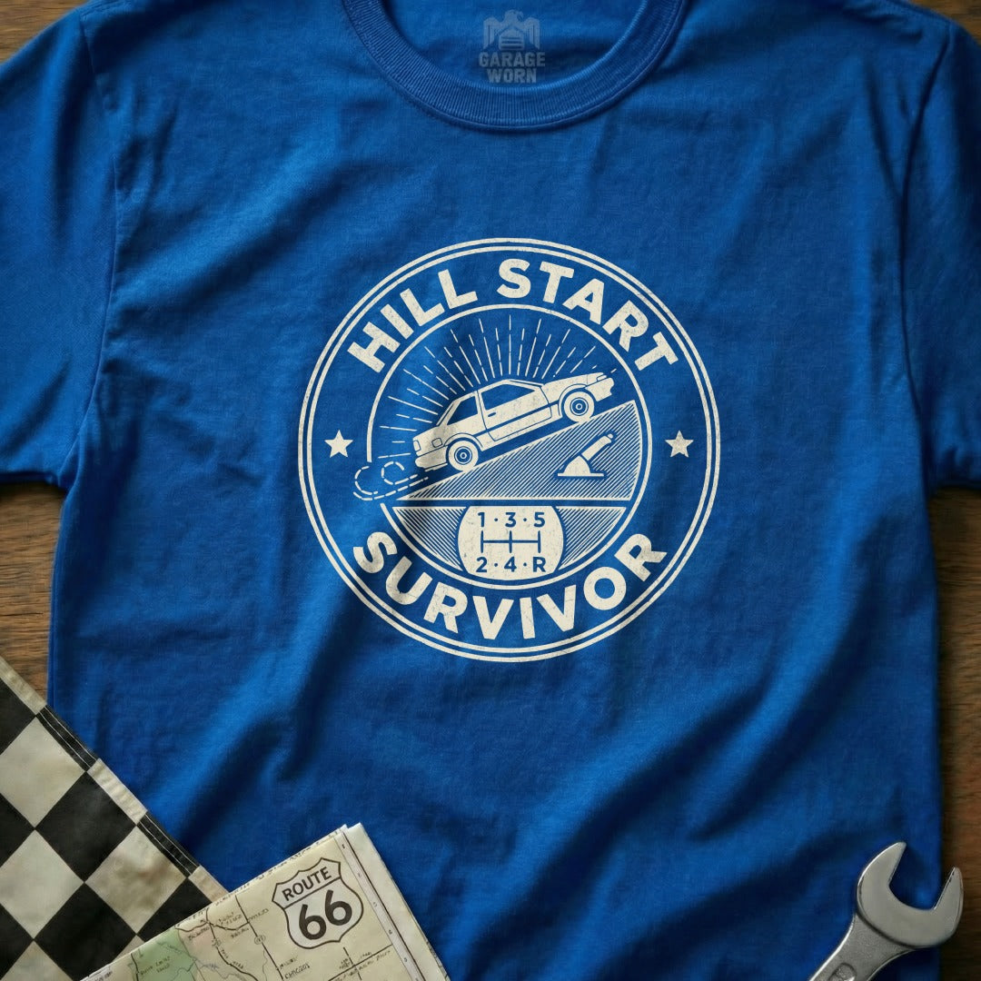 Blue t-shirt with "Hill Start Survivor" graphic and car on a steep incline.