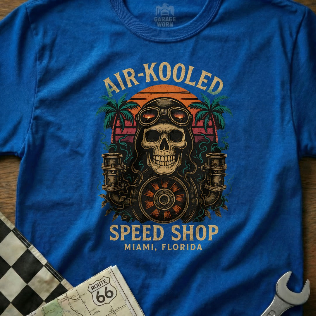 Blue t-shirt with graphic of skull wearing goggles, gears, and palm trees.