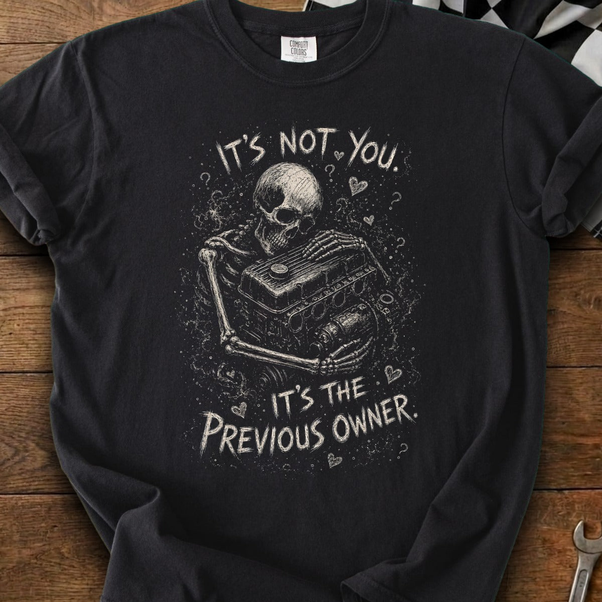 Black t-shirt with skeleton holding car engine design and text "It's not you. It's the previous owner."