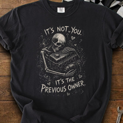 Black t-shirt with skeleton holding car engine design and text "It's not you. It's the previous owner."