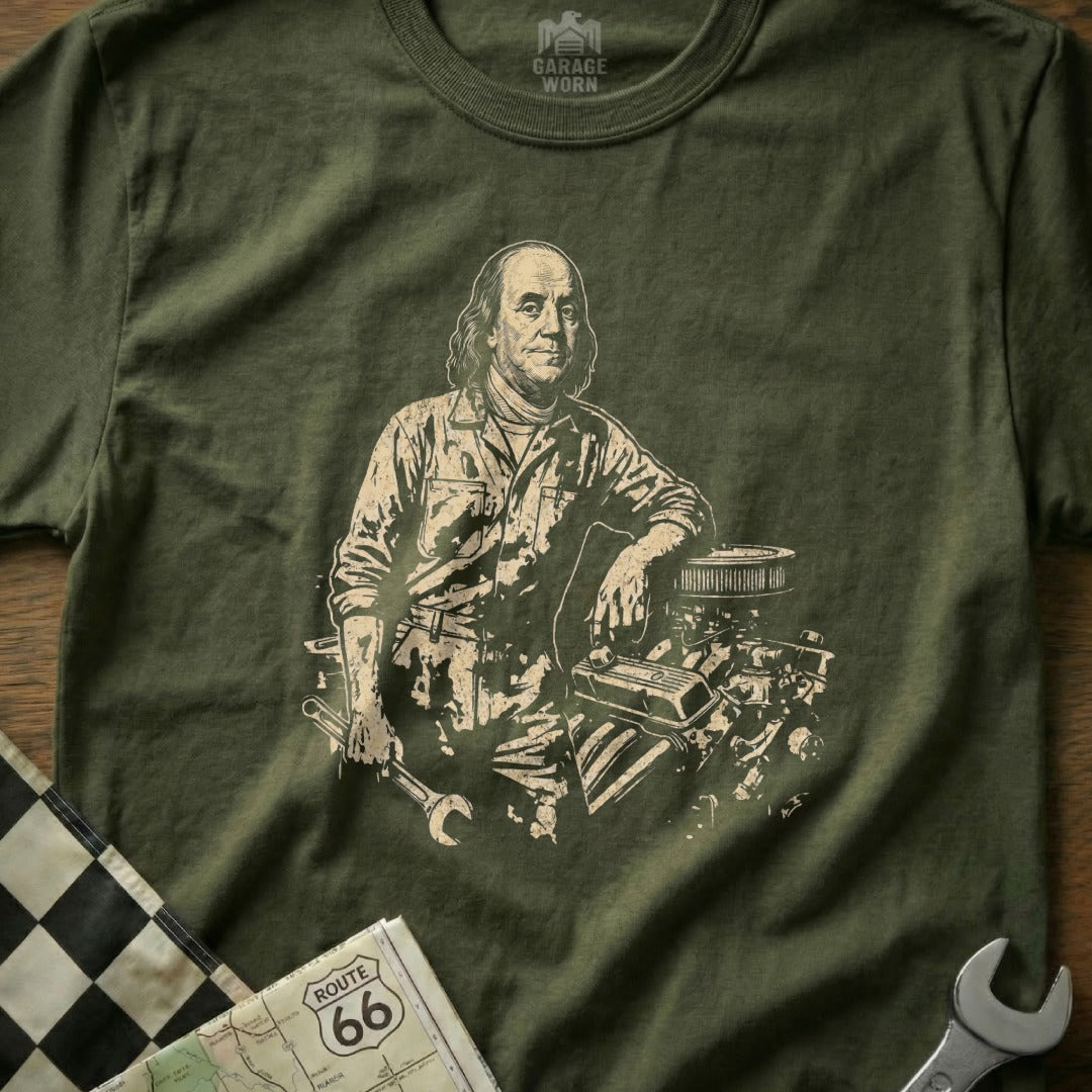 Benjamin Franklin leaning on an engine with tools, on a green t-shirt.